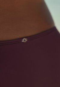 Burgundowe bikini dolne o gładkiej fakturze, z małym metalicznym logo na linii talii.