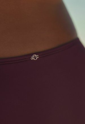 Burgundy bikiniunderdel med en slät textur, med en liten metallisk logotypaccent vid midjan.