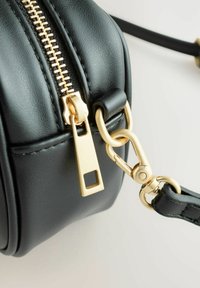 Zwarte leren handtas met een gouden rits, metalen gesp en een gestructureerde afwerking. Heeft een afgeronde vorm en een smalle riemophanging.