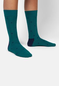 Des chaussettes turquoise avec des pois bleu marine, une bordure côtelée et un talon bleu marine contrastant. Fabriquées dans un tissu doux et extensible.