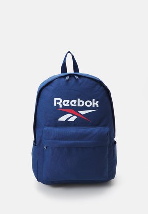 Mochila de tela azul marino con el logo de Reebok en blanco y rojo. Cuenta con un compartimento principal, un bolsillo frontal y dos asas superiores.