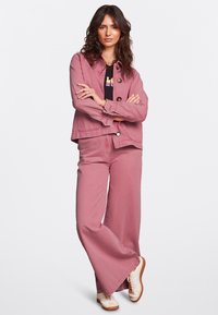 Chaqueta de mezclilla rosa con grandes botones, combinada con pantalones de pierna ancha a juego y una camiseta gráfica negra. Zapatillas de color crema completan el look.