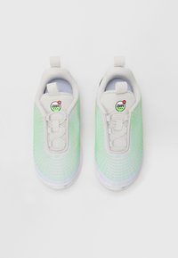 Balti un neona zaļi Nike Air Max tenisi, skatīti no augšas uz baltas fona, bez redzamām šņorēm.