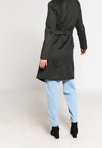 Ciemnoszary, długi płaszcz o gładkiej fakturze, z paskiem w talii i wysokim kołnierzem. Połączony z jasnoniebieskimi dżinsami i czarnymi botkami za kostkę.