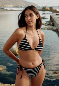 Črno-bela bikinija s črtami vsebuje trohoekast vrh z tankimi trakovi in bokovim delom na zavezovanje, izdelan iz rebraste teksturirane tkanine.