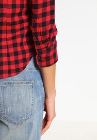 Röd och svart rutigt flanellskjorta med knäppta manschetter, bärs över blå denimjeans, vilket visar en avslappnad och ledig passform.