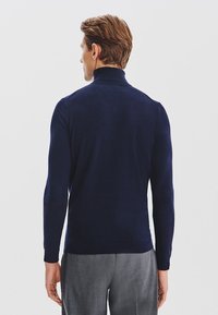 Granatowy, dopasowany sweter z golfem wykonany z miękkiej, dzianinowej tkaniny, z prążkowanym kołnierzem i mankietami, noszony z jasnoszarymi spodniami.