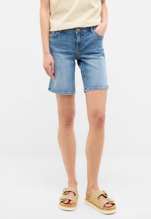 Shorts en denim bleu clair, taille mi-haute avec une coupe droite, comportant cinq poches, des détails de couture et un ourlet retroussé. Associés à des sandales beiges.