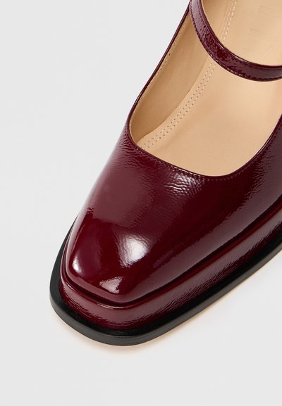 Μπορντό παπούτσι Mary Jane από πατεντέ δέρμα με τετράγωνη μύτη, στρογγυλή λωρίδα στον αστράγαλο και μαύρη καουτσούκ σόλα. Λείο φινίρισμα με ραφές.
