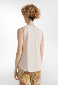 Top sin mangas de color rosa claro con escote redondo y un pequeño detalle de cremallera en la parte trasera. Textura suave de algodón. Combinado con pantalones estampados.