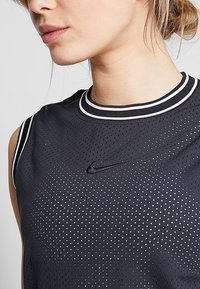 Czarny bezrękawnik sportowy z teksturowanym siateczkowym wzorem, okrągły dekolt z białymi paskami oraz małym czarnym logo Nike na klatce piersiowej.