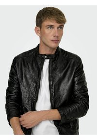 Zwarte leren jas met een gewatteerd schouderontwerp, drukknopenkraag en ritssluiting, gecombineerd met een wit T-shirt met ronde hals eronder.