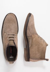 Chaussures brunes et texturées en matériau ressemblant à des cheveux. Design à lacets avec un bout arrondi et une semelle foncée contrastante. Détails de couture remarquables.