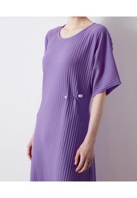 Lila, geripptes Kleid mit rundem Ausschnitt und kurzen Ärmeln, mit einer dekorativen Brosche mit zwei dekorativen Perlen an der Seite.