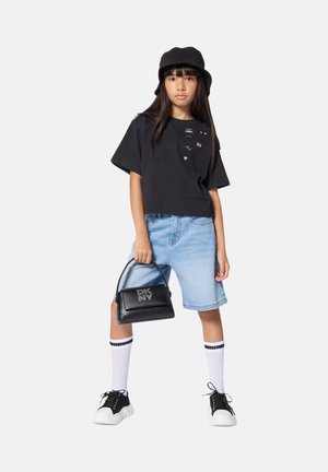 T-shirt noir court avec accents graphiques, short en denim bleu clair, sac à main noir avec logo, chaussettes blanches à rayures noires, et baskets noires.