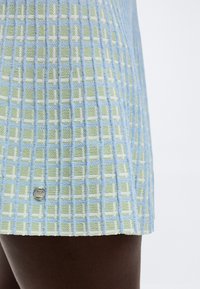 Κοντινή λήψη πλισέ φούστας με μπλε και πράσινο καρό μοτίβο, φορεμένη σε σκουρόχρωμο δέρμα.