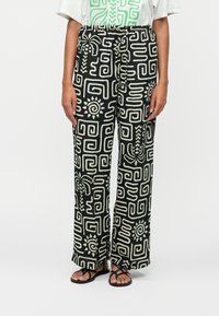 Pantalon large noir avec des motifs géométriques crème, taille élastique et tissu léger, présentant des motifs de soleil et de plantes.