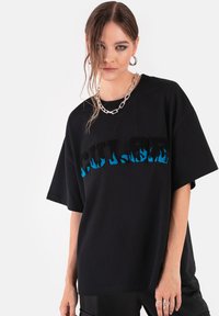 Czarna, oversize koszulka z krótkim rękawem, z niebieskim wzorem płomieni na teksturze napisu "COLOR". Okrągły dekolt i miękki materiał bawełniany.
