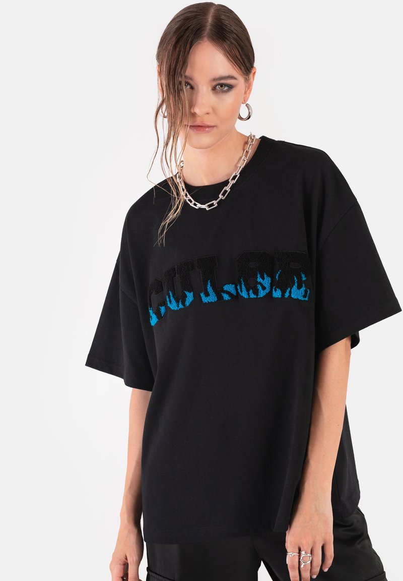 Czarna, oversize koszulka z krótkim rękawem, z niebieskim wzorem płomieni na teksturze napisu "COLOR". Okrągły dekolt i miękki materiał bawełniany.