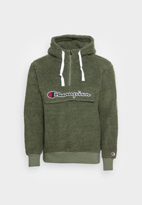Felpa in pile verde oliva con mezza zip, lacci bianchi, patta della tasca frontale e logo "Champion" sul petto e sul polso.