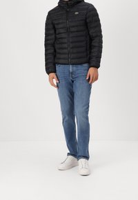 Černá péřová bunda s vodorovným prošíváním, zapínáním na zip a kapucí. Nošena s modrými džínami a bílými teniskami, s zeleným logem na hrudi.