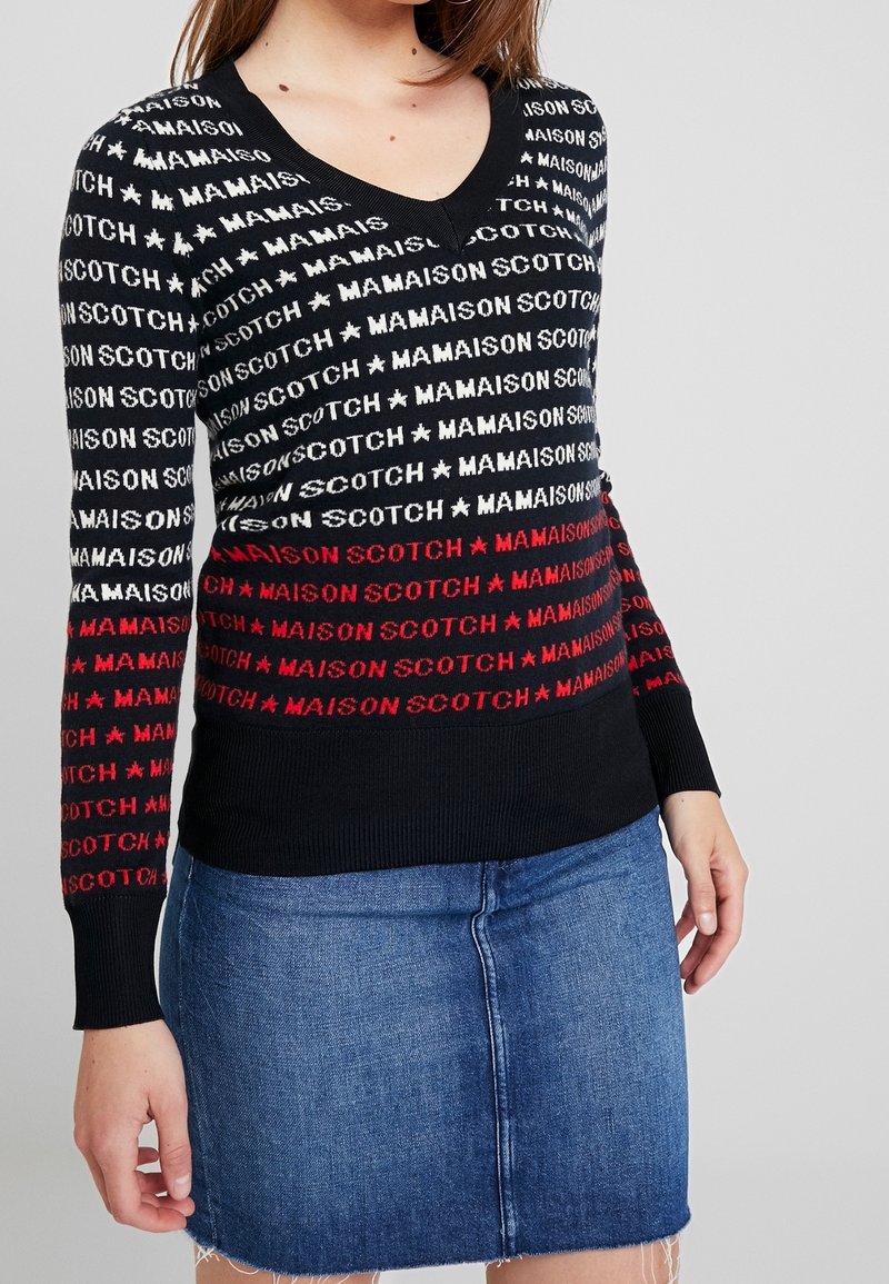 Czarny sweter dzianinowy z powtarzającym się napisem "MAISON SCOTCH" w kolorach czerwonym i białym, dekolt w serek, długie rękawy i ściągacz na dole.