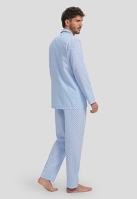 Conjunto de pijama azul claro que incluye una camiseta de botones de manga larga y pantalones a juego, ambos decorados con pequeños lunares negros.