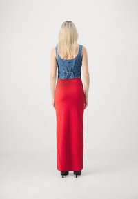 Top en denim court avec dos ajustable, associé à une longue jupe rouge à pois. La tenue est complétée par des talons hauts et une texture lisse.