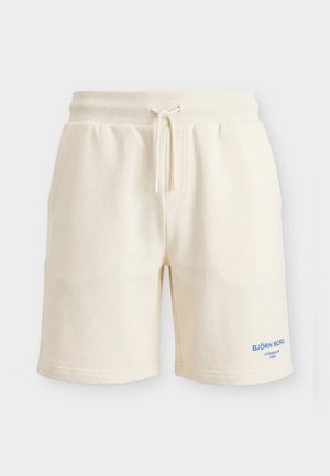 Pantaloni scurți casual de culoare crem, cu talie elastică și șnur, buzunare laterale și text albastru „BJÖRN BORG STOCKHOLM 1956” pe piciorul stâng.