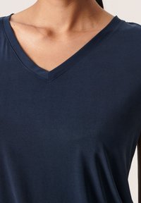 Námořnická vesta bez rukávů s V výstřihem vyrobená z hladkého, lehkého materiálu s jemnou texturou. Má čisté zakončení kolem výstřihu a ramen.