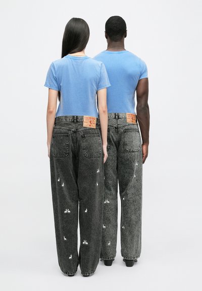 Mörkgrå baggy jeans med vit kaninbroderi, med en blekt textur och orange etiketter. Matchas med blå åtsittande t-shirts.