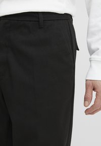Svart bukser med en jevn tekstur og en slim fit-design. Har en diskret fronlomme og en matchende beltehempe i midjen.