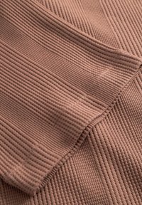 Detailní záběr složené hnědé žebrované pleteniny zobrazující texturované vertikální a horizontální linie a detail švu.