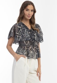 Sort og beige slangeprint peplum bluse med flagrende ærmer og v-udskæring, lavet af letvægts, gennemsigtigt stof. Bæres med hvide bukser.