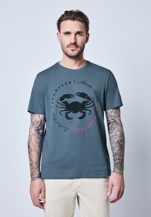 Graues Baumwoll-T-Shirt mit Rundhalsausschnitt, das ein schwarzes Krebs-Motiv und den Text "Atlantic Breeze" in Rot zeigt. Es hat kurze Ärmel und eine lockere Passform.