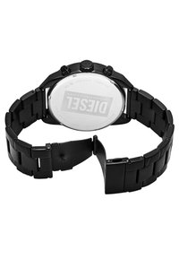 Montre en acier inoxydable noir avec un bracelet en maille poli, trois boutons chronographes sur le côté et un dos transparent affichant le logo.