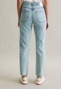 Lichtblauwe high-waisted jeans met een rechte pasvorm, zichtbare achterzakken en een licht vervaagde textuur. G gedragen met witte sneakers.