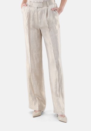 Frau trägt hochgeschnittene, weite beige Leinenhose mit vorderen Falten und Händen in den Taschen, kombiniert mit beigen spitzen Absätzen.