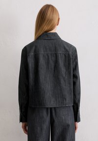 Czarna kurtka dżinsowa z kołnierzem, długimi rękawami i zapinanymi na guziki mankietami. Tkanina ma subtelną fakturę z delikatnym połyskiem.