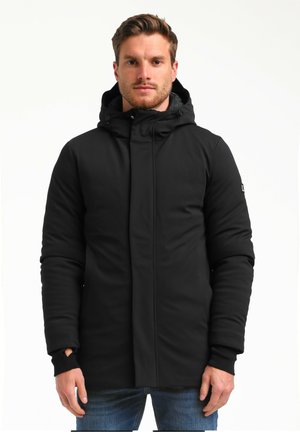 Chaqueta aislante negra con capucha, cremallera frontal y puños con orificio para el pulgar, fabricada con un material liso y mate. Diseño minimalista.
