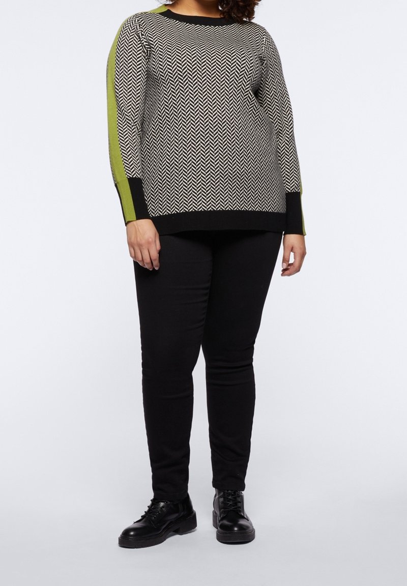 Black and white patterned sweater with herringbone design, green accent stripes on sleeves, paired with black slim-fit pants and black shoes.