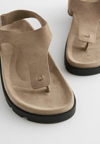 Beige suède teensandalen met een gestructureerd oppervlak, minimalistisch ontwerp en een zwarte rubberen zool voor grip.