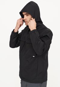 Schwarze Kapuzenjacke mit zwei vorderen Taschen, elastischen Bündchen und einem Reißverschluss. Leichter Stoff mit einem strukturierten Muster.