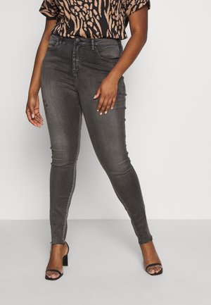 Kobieta w czarnych, wyblakłych, obcisłych jeansach z wysokim stanem, połączonych z czarnymi sandałami z odkrytymi palcami i brązowo-czarną bluzką w zwierzęcy wzór.