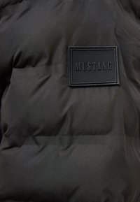 Czarna podszyta kurtka z teksturowaną prostokątną łatą z napisem "MUSTANG" przyszytą do tkaniny.