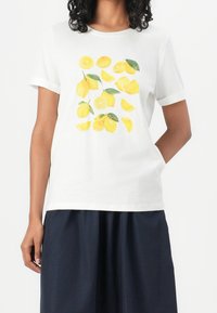 Weißes Baumwoll-T-Shirt mit kurzen Ärmeln und gelbem Zitronenmotiv. Das Design zeigt ganze und geschnittene Zitronen mit grünen Blättern.