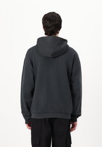 Dark gray oversized hoodie made from cotton blend, featuring a drawstring hood, ribbed cuffs, and a relaxed fit. The back view is shown.