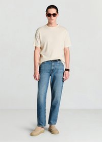 Beige geripptes T-Shirt mit kurzen Ärmeln, blaue Jeans mit geradem Bein, beigefarbene Slipper und dunkle Sonnenbrille. Einfaches, lässiges Outfit bei einem Mann.
