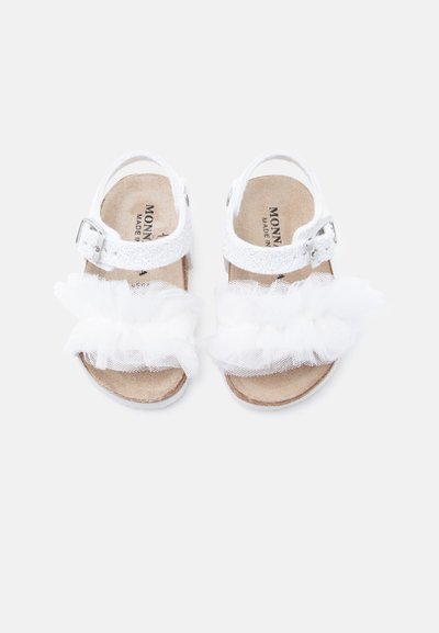 Λευκά παιδικά σανδάλια με υφασμένη λωρίδα, ασημένια αγκράφα και διακοσμητικό λευκό βολάν από τούλι στην περιοχή των δακτύλων.