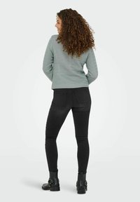 Ljusgrön texturerad tröja i kombination med svarta skinny jeans och svarta ankelboots med spännen, sedd bakifrån.